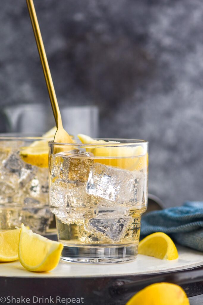 glass of gin and ginger ale with ice and lemon being stirred