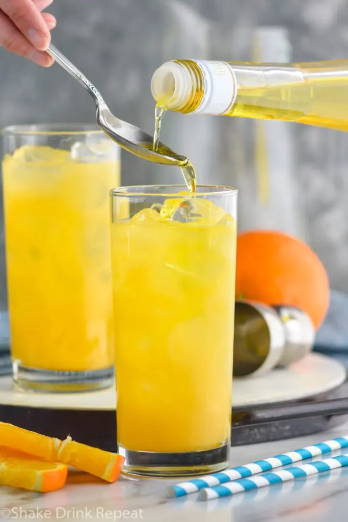 making a Harvey Wallbanger drink recipe with Galliano poured into glass with orange wedge garnish