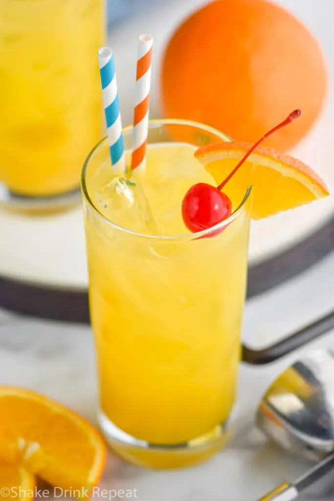 Glass of Harvey Wallbanger drink with straws, orange wedge and cherry garnish