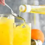 making a Harvey Wallbanger drink recipe with Galliano poured into glass with orange wedge garnish