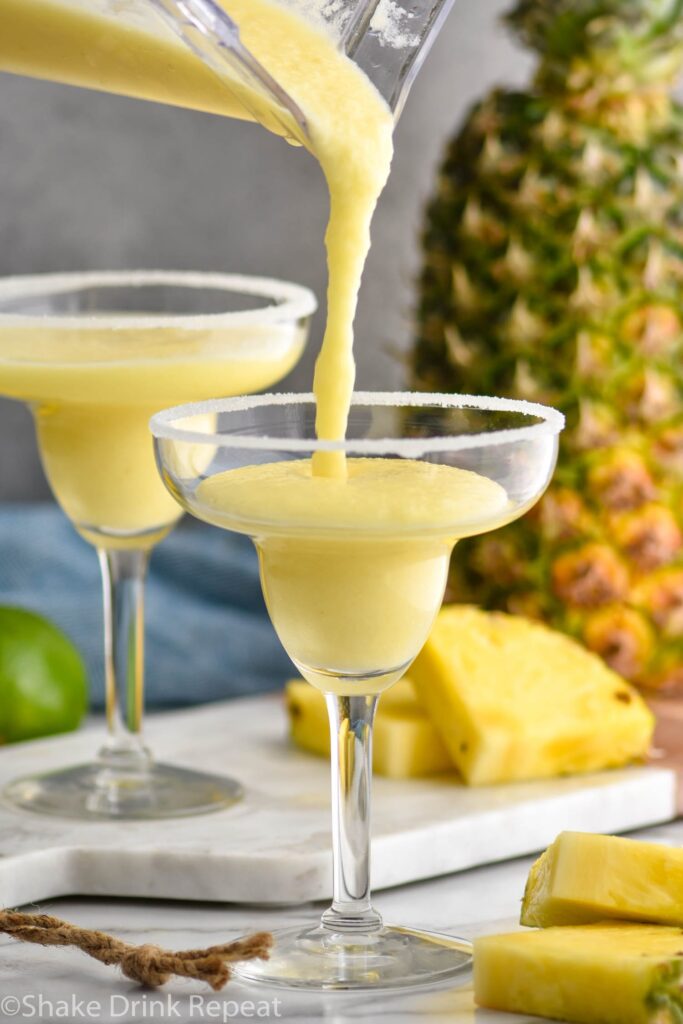 two glasses pineapple margarita recipe being poured with salted rim