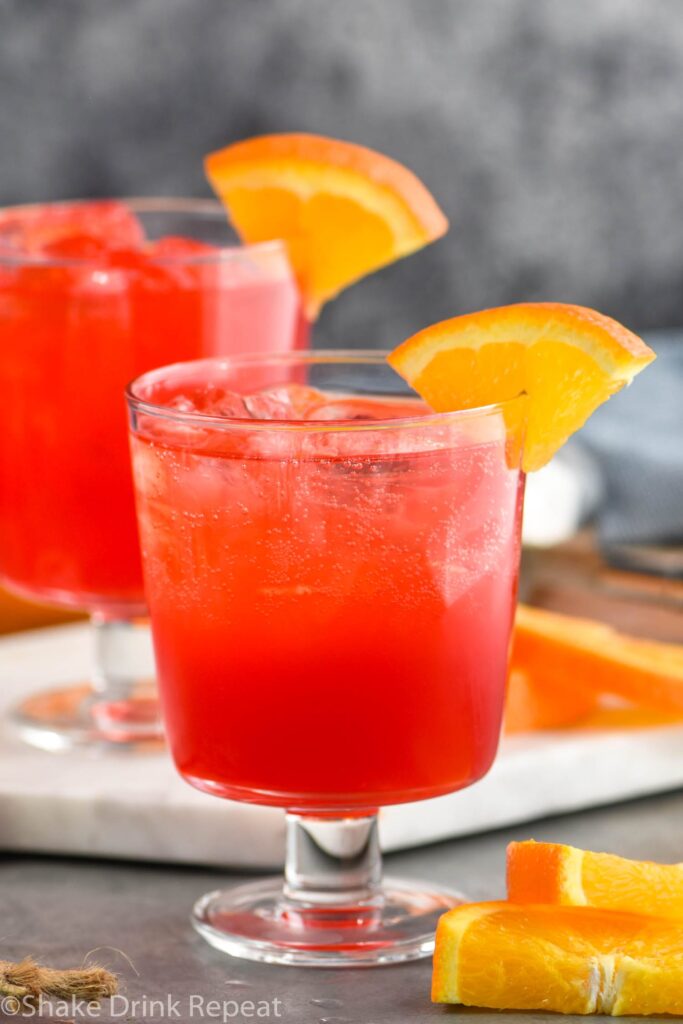 two glasses of sloe gin fizz with ice and orange slice garnish