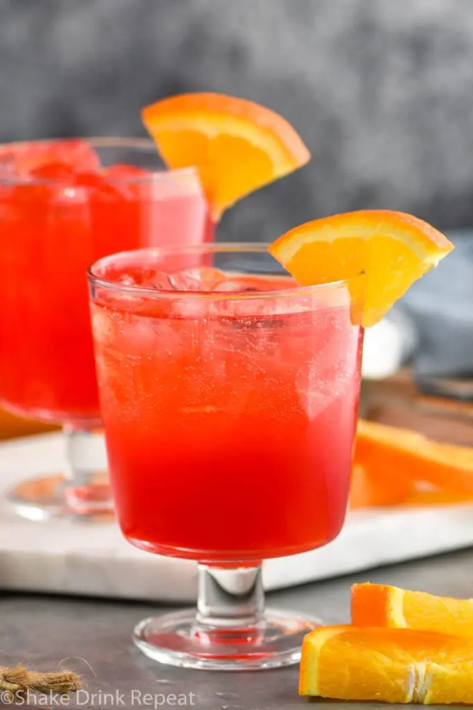 two glasses of sloe gin fizz with ice and orange slice garnish