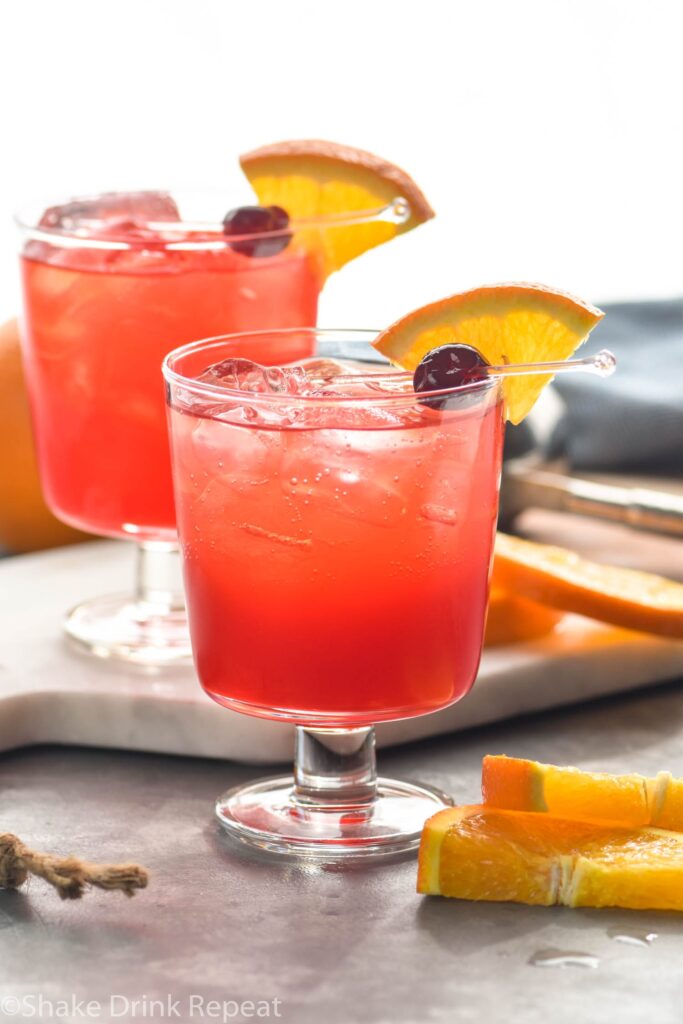 two glasses of sloe gin fizz cocktail with orange slice and cherry garnish