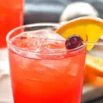 Glass of sloe gin fizz recipe with orange slice and cherry garnish