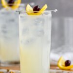 glass of tom collins cocktail with ice, cherry and lemon slice