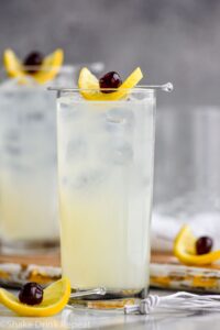 glass of tom collins cocktail with ice, cherry and lemon slice