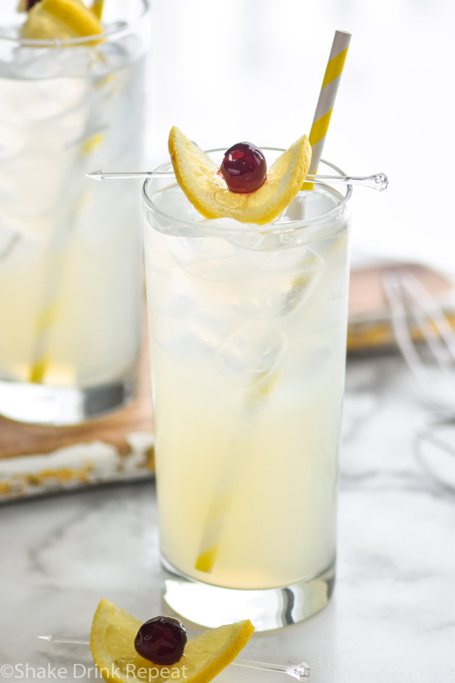 two glasses tom collins cocktail with ice, lemon, and cherry
