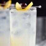 glass of tom collins drink with ice, lemon and cherry
