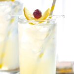 glass of tom collins drink with ice, lemon, and cherry