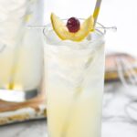 glass of tom collins with ice, lemon and cherry garnish