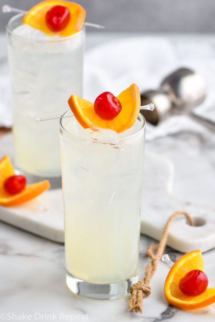 two glasses of vodka collins with ice, orange slice and cherry