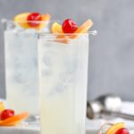 two glasses of vodka collins with ice, orange slice and cherry garnish