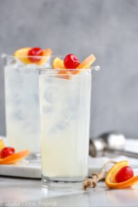 two glasses of vodka collins with ice, orange slice and cherry garnish