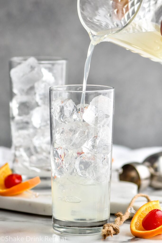 glass of vodka collins ingredients with ice, orange slice and cherry garnish