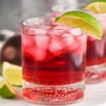 Glass of Vodka Cranberry with ice and lime wedge and recipe ingredients in background