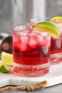 Glass of Vodka Cranberry with ice and lime wedge and recipe ingredients in background
