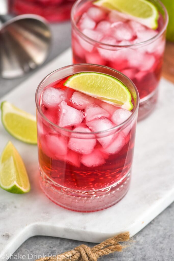 two glasses of vodka cranberry recipe with ice, lime wedges and jigger in background