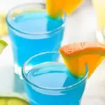 two shot glasses kamikaze shots with orange and lime wedges