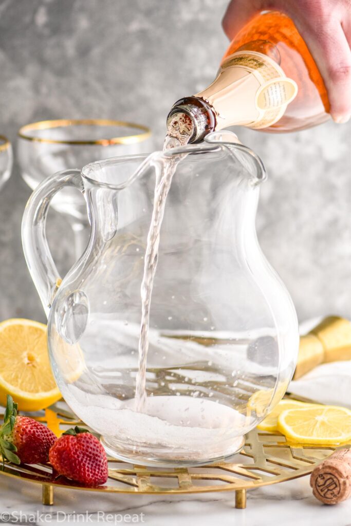Mimosa Sangria ingredients in glass pitcher with orange slices and strawberries