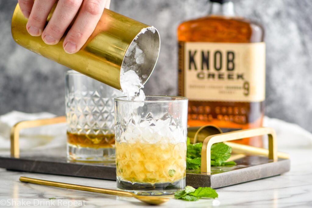 Making mint julep cocktail with shaved ice, bourbon and mint leaves