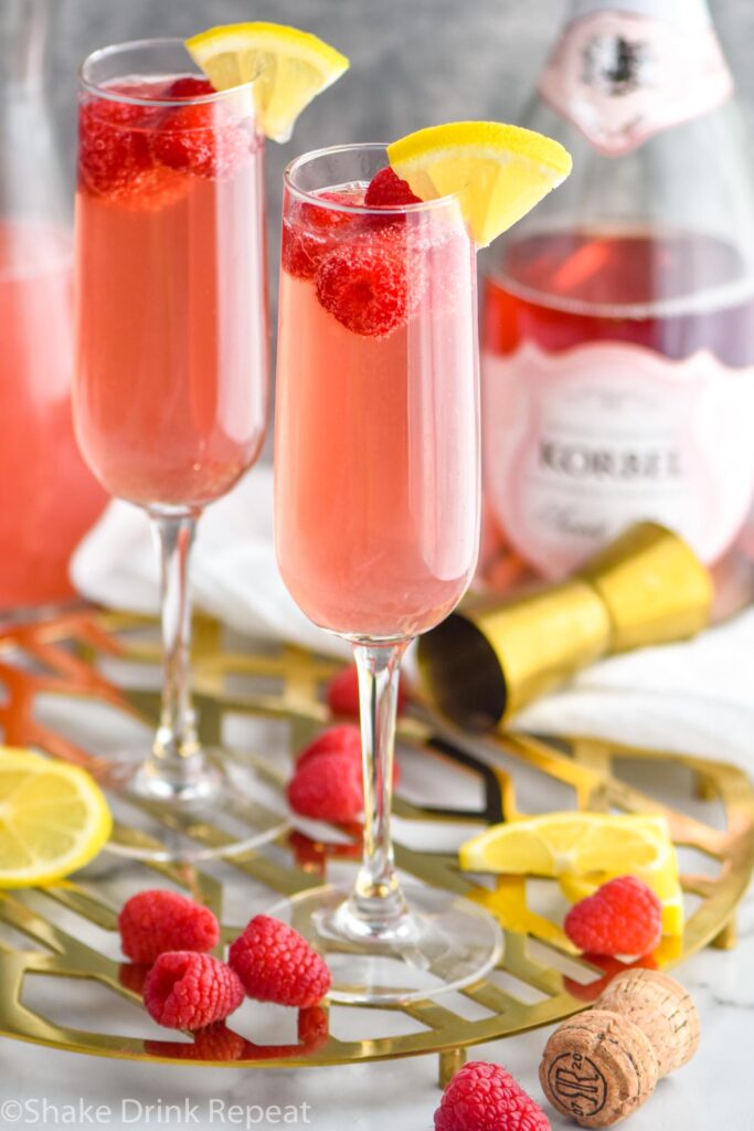 two glasses of pink mimosa recipe with ingredients and fresh raspberries and lemon slices