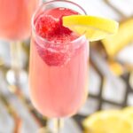 glass of pink mimosa with lemon slice and raspberries