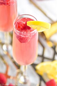 glass of pink mimosa with lemon slice and raspberries