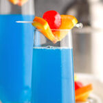 two glasses of blue kamikaze recipe with orange and cherry garnish