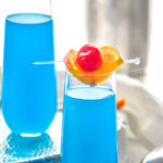 two glasses of blue kamikaze recipe with orange and cherry garnish