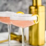 two glasses of cranberry gin fizz with lemon twist and shaker in background