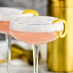 two glasses of cranberry gin fizz with lemon twist and shaker