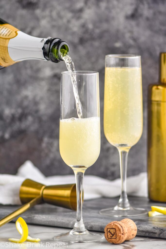 pouring champagne into a glass of french 75 with lemon twist