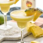 two sugar rimmed glasses of blended malibu pineapple margarita with pineapple garnish