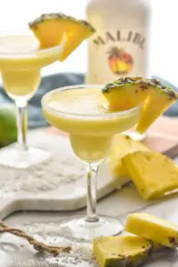 two sugar rimmed glasses of blended malibu pineapple margarita with pineapple garnish