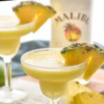 two sugared rim glasses of malibu pineapple margarita with coconut garnish