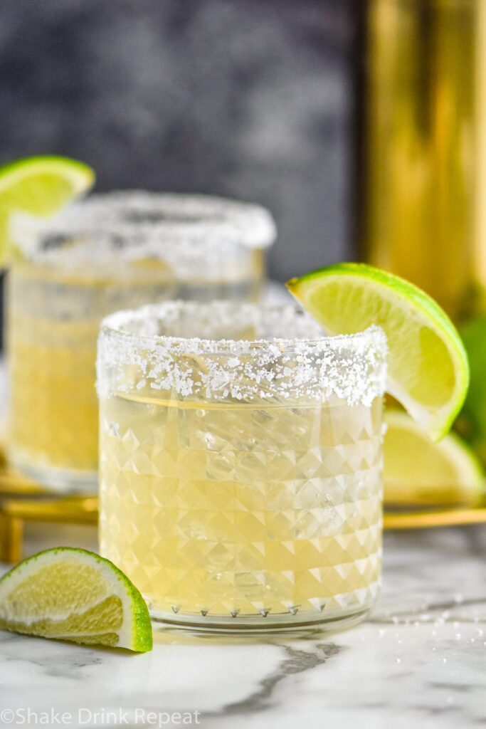 two glasses of margarita with salted rim, ice, and lime