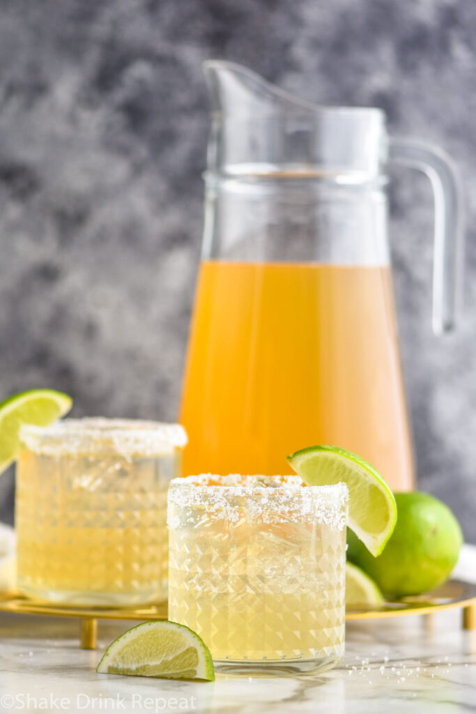 pitcher and two glasses of margarita with salted rim, ice, limes