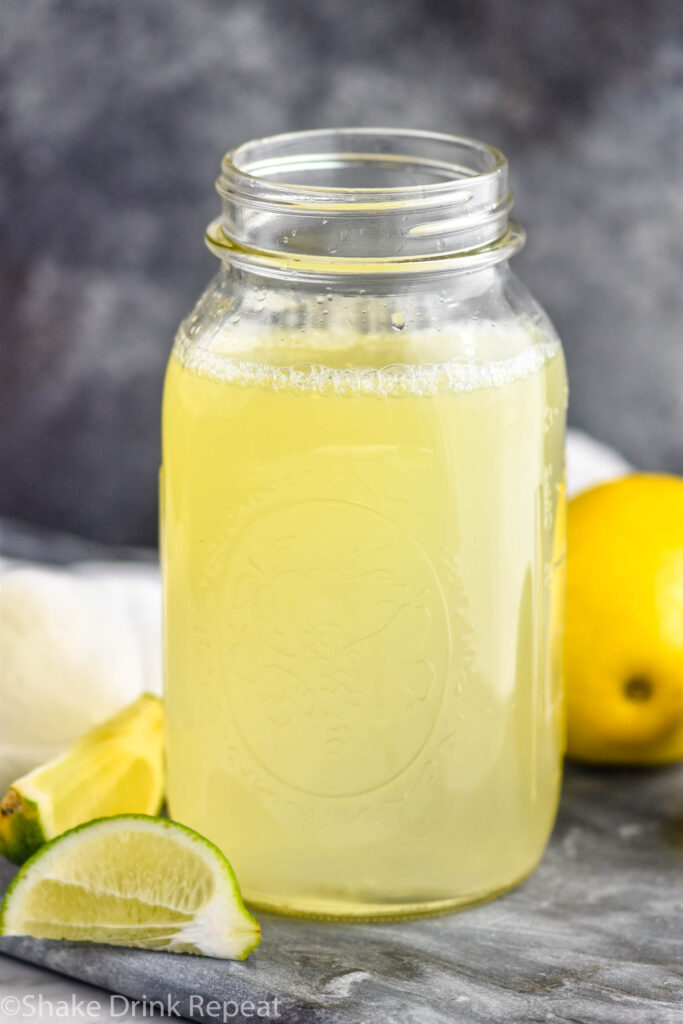 jar of homemade margarita mix with lemons and limes.