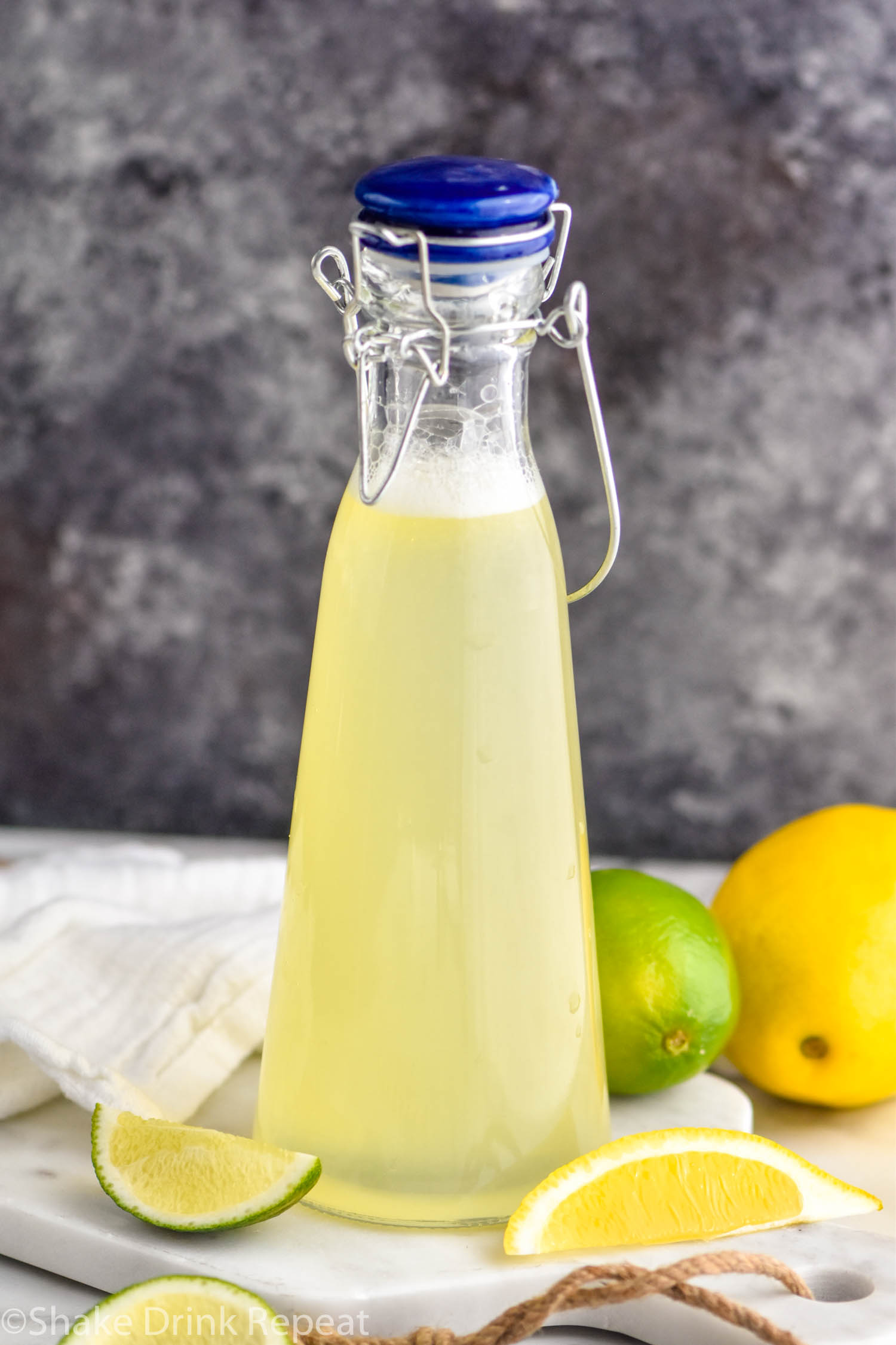 bottle of homemade margarita mix with fresh lemons and limes