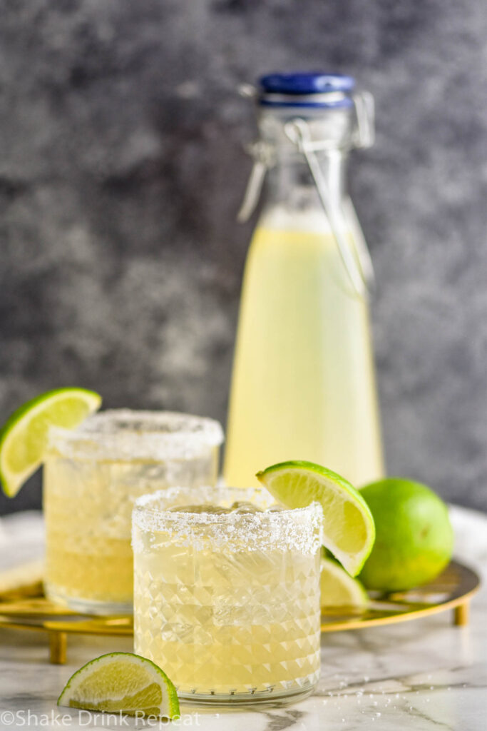 two salt rimmed glasses of margaritas made with homemade margarita mix surrounded by lemons and limes