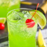 glass of midori sour cocktail with ice, lime, and cherry