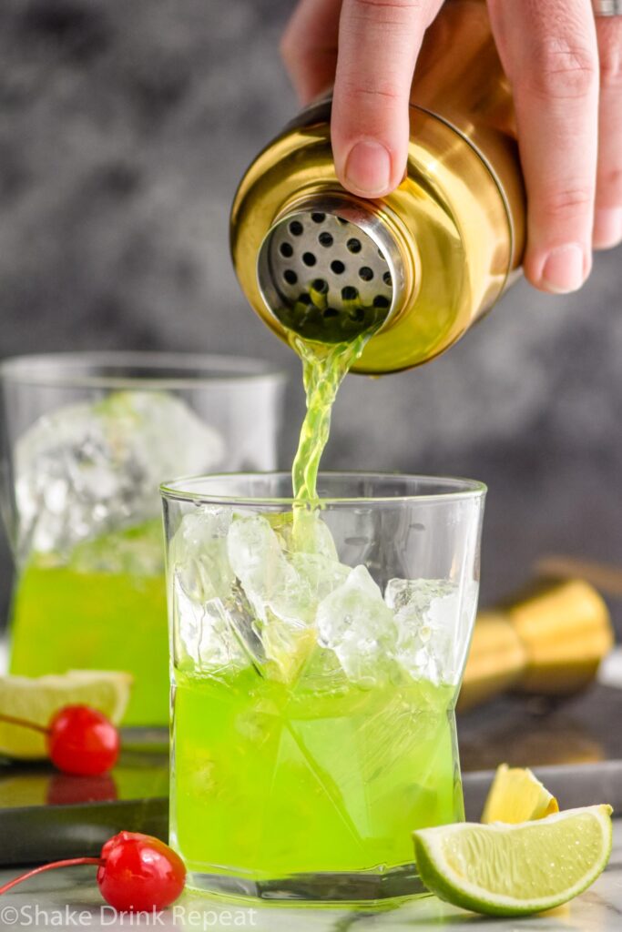 making a midori sour in a shaker and pouring into a glass with ice, lime, and cherry