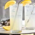 two glasses of rum collins with ice, lemons and straws.