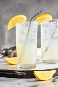 two glasses of rum collins with ice, lemons and straws.