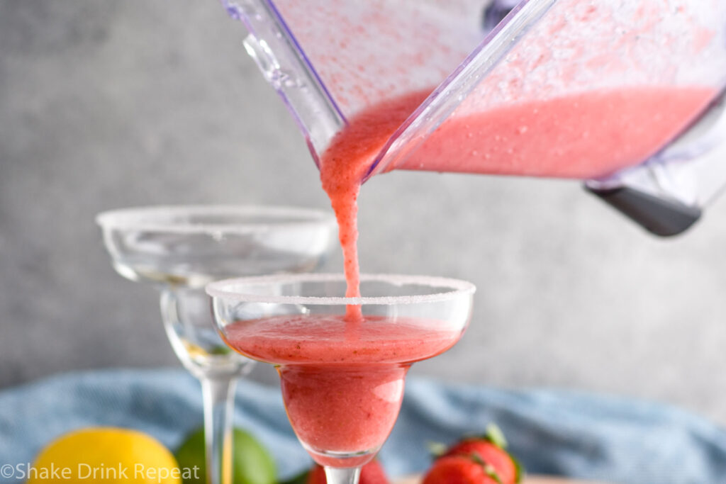 pouring frozen strawberry margarita from a blender into a glass with sugared rim