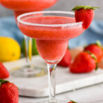 two glasses of frozen strawberry margarita with sugared rim and fresh strawberries