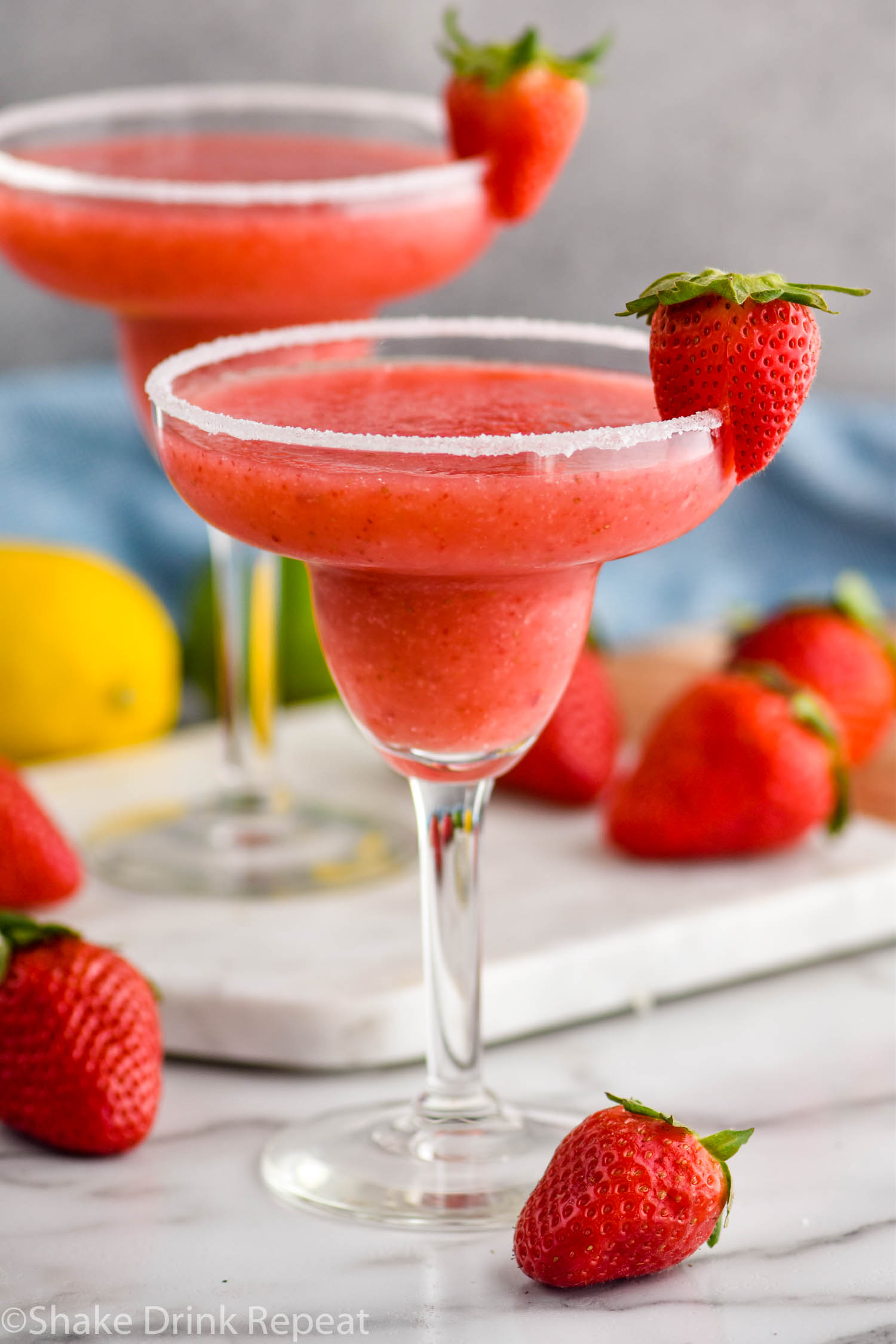 two glasses of frozen strawberry margarita with sugared rim and fresh strawberries