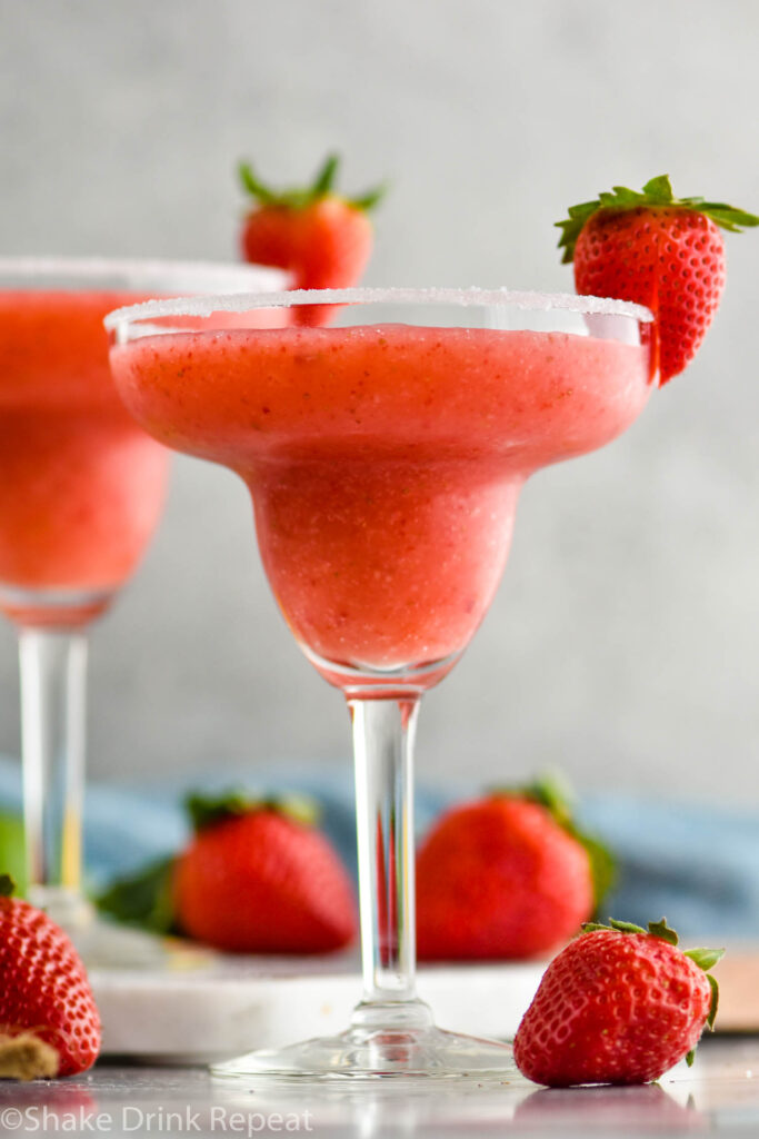 two glasses of frozen strawberry margarita with sugared rim and fresh strawberries