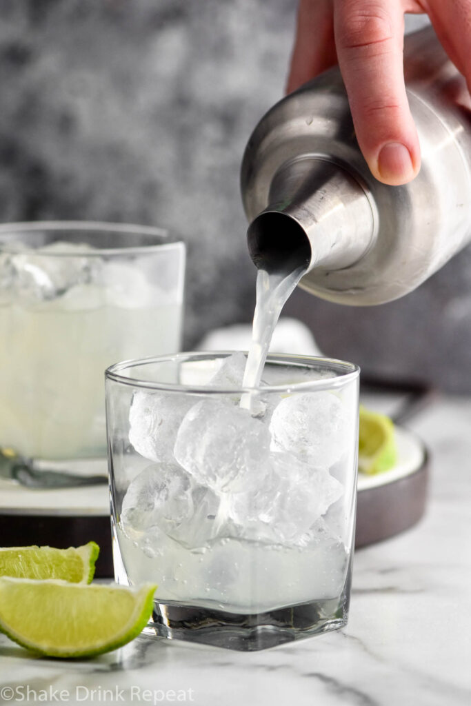 making a vodka gimlet recipe with a shaker in a glass with ice and limes